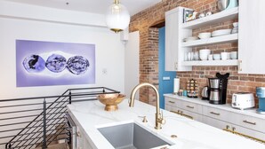 A modern kitchen with a white countertop, a sink with a gold faucet, a coffee machine, and a shelf with dishes. - NEW! Brush Park Brilliance! Walk->Stadiums DT Luxe 3BR (Detroit)