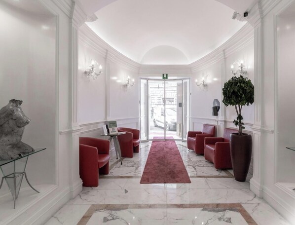 Een hotellobby met marmeren vloeren, rode zitplaatsen, een groot rood tapijt en een grote potplant.