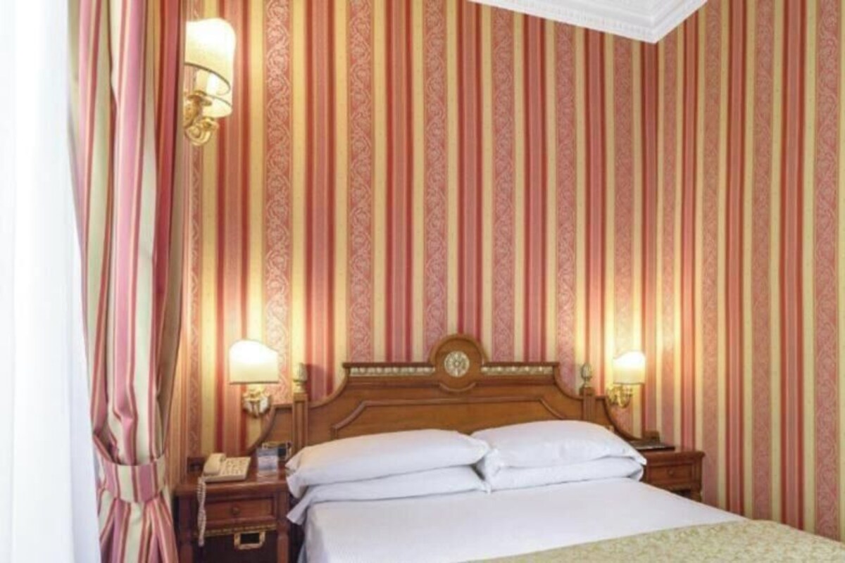 Een hotelkamer met een groot bed, twee nachtkastjes en een muur met verticale strepen.