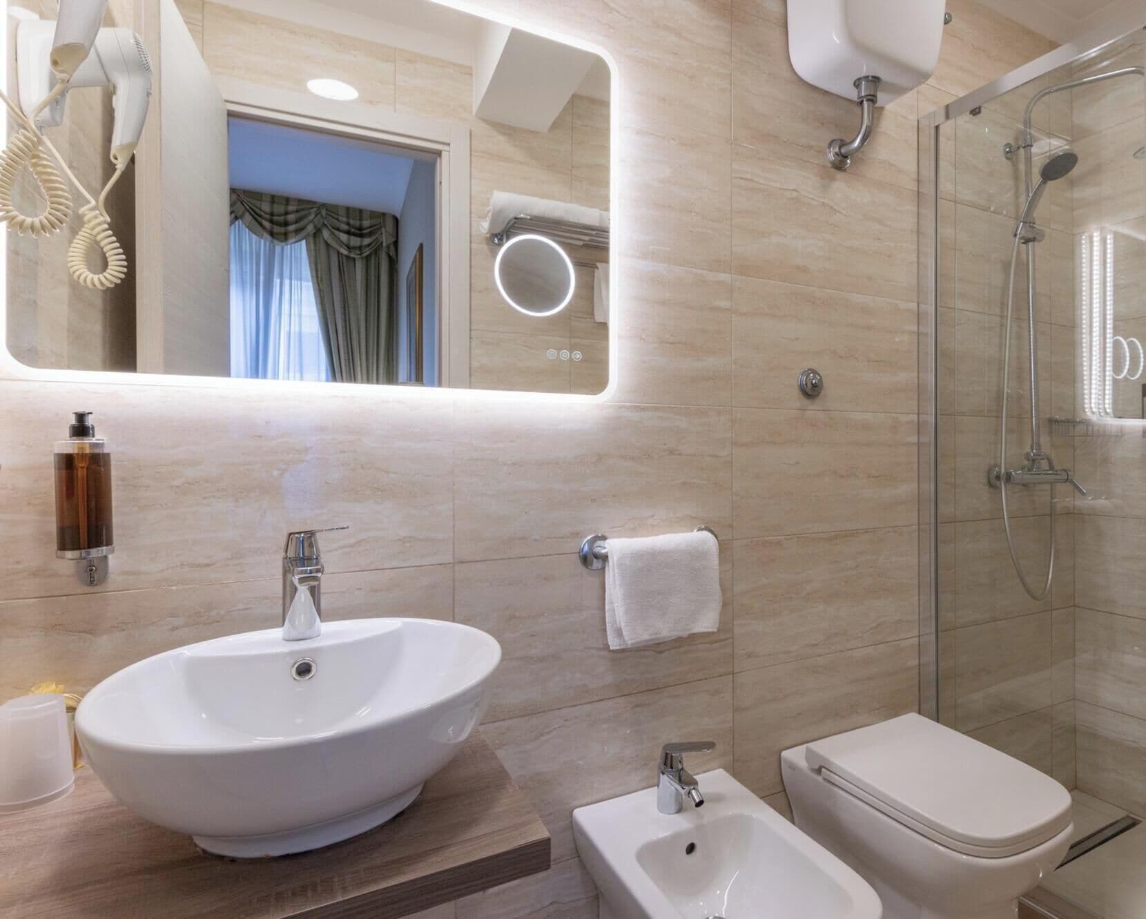 Une salle de bain moderne dotée d’un grand lavabo ovale, d’un autre lavabo sur pied, d’une douche à parois de verre et d’un miroir avec éclairage intégré.