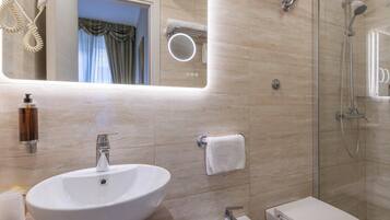 Une salle de bain moderne dotée d’un grand lavabo ovale, d’un autre lavabo sur pied, d’une douche à parois de verre et d’un miroir avec éclairage intégré.