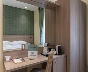 Een hotelkamer met een bed, een bureau met een bordje, een koffieapparaat en een kast.