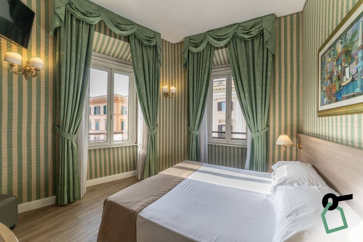 Une chambre d’hôtel avec un grand lit, un papier peint à rayures et deux fenêtres avec des rideaux.