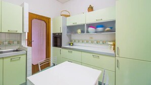 A compact kitchen with light green cabinets, a white countertop, and a small table. - Villa Mimma (Sant'Agnello)