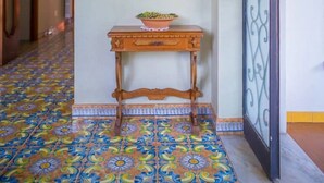 A hallway with a tiled floor, a wooden table with a bowl, a vase with flowers, and a decorative wall. - Villa Mimma (Sant'Agnello)