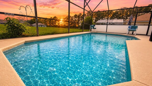 Una piscina rettangolare con superficie d'acqua blu trasparente, circondata da un solarium color beige.