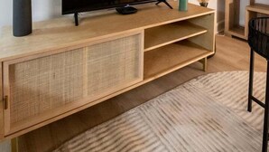 Un salon moderne avec un grand téléviseur à écran plat posé sur une console en bois, un meuble en rotin tressé en dessous, et un tapis à motifs sur le sol.