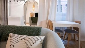 Un salon moderne avec un canapé, un miroir rond, une table à manger avec des chaises et une fenêtre avec des rideaux.