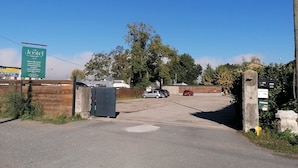 A gated entrance to a property with a signboard, a parking area, and a building in the background. - Le Jostel 5 _ Chemin de la petite Rive (Genay)