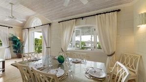 Un coin repas avec une table ronde dressée pour quatre personnes, entourée de chaises, et offrant une vue sur l’extérieur grâce à de grandes fenêtres.