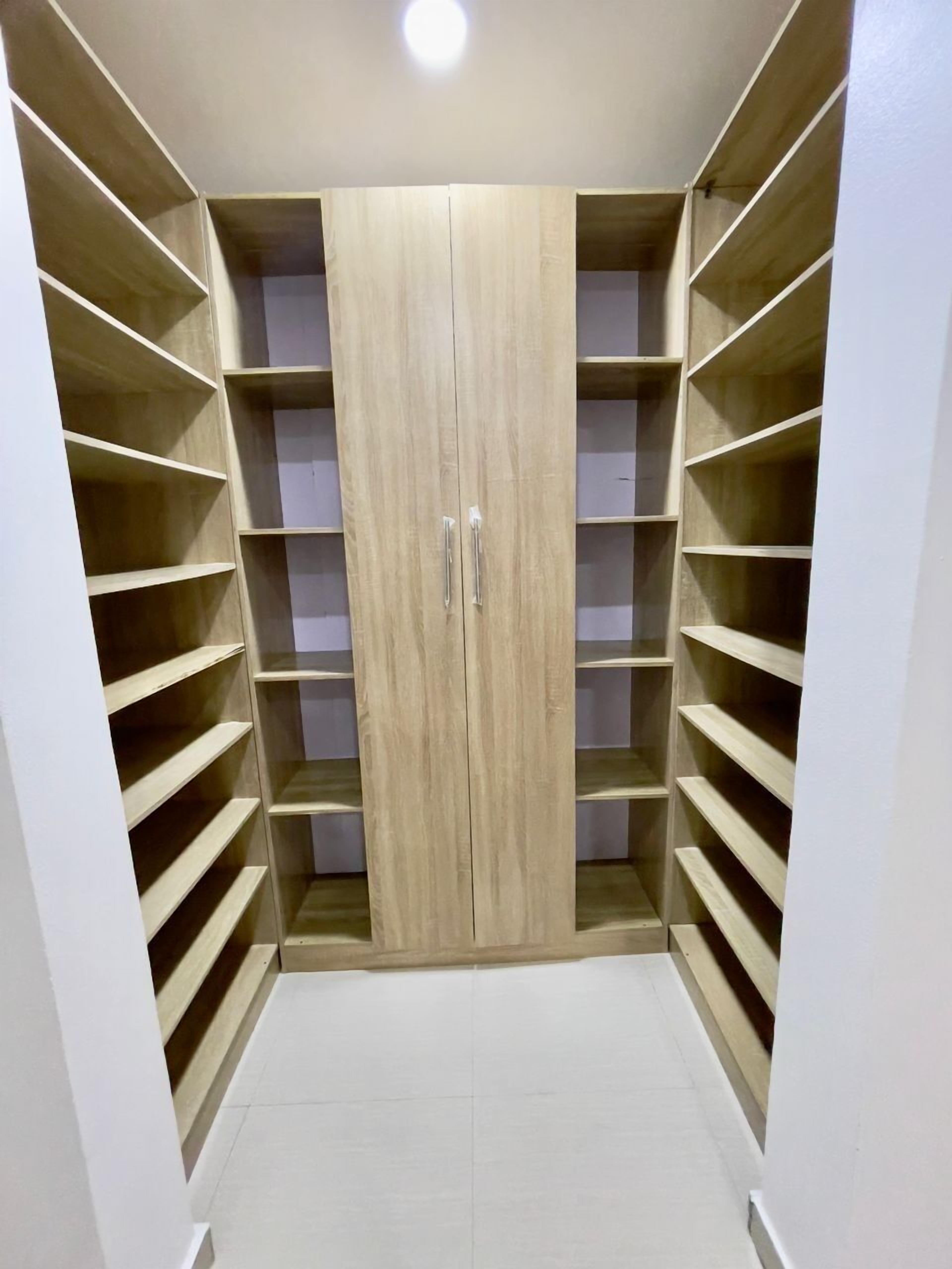 A walk-in closet with wooden doors and multiple shelves.