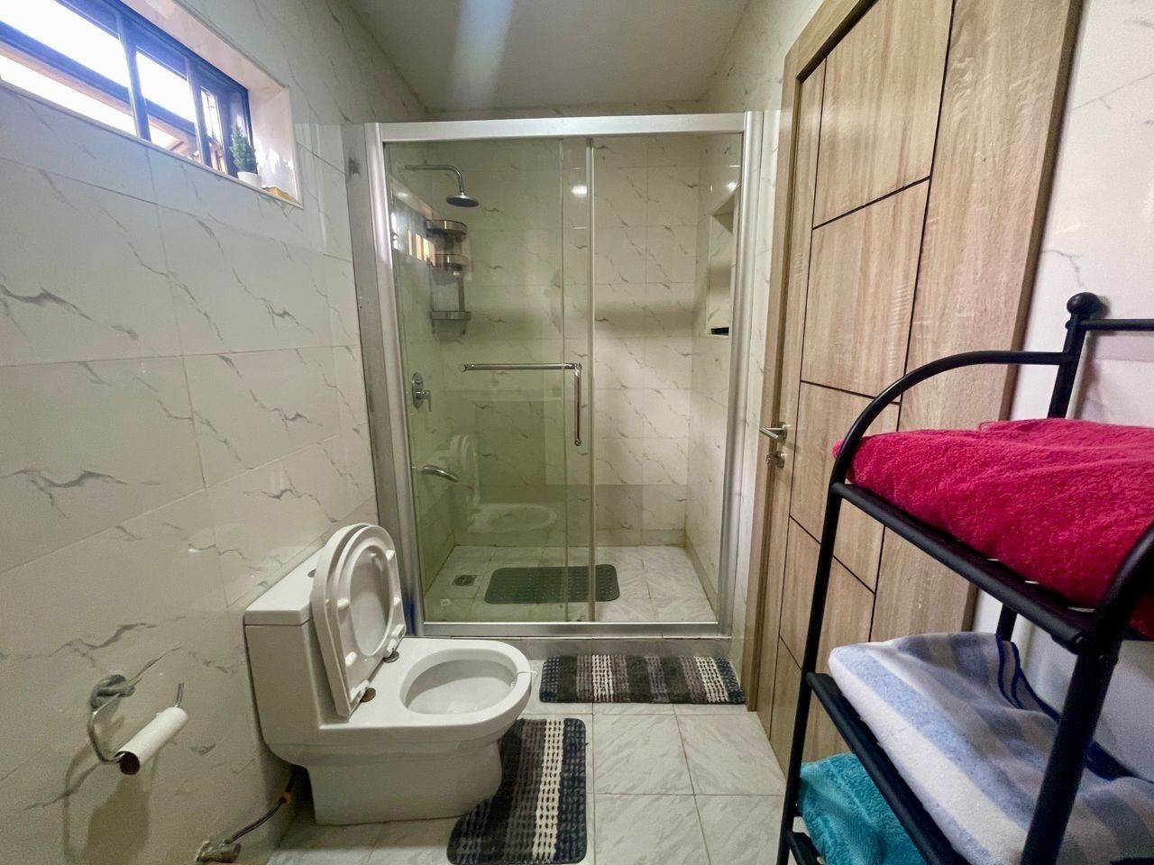 Een badkamer met toilet, douche en een stapelbed met een rode handdoek.