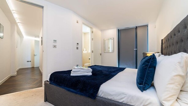 Une chambre moderne avec un grand lit, une tête de lit sombre et une vue sur un couloir.