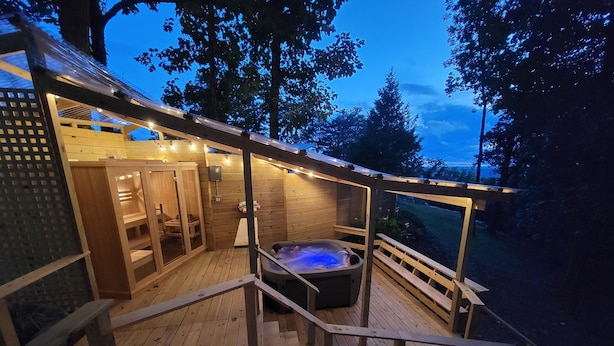 A wooden deck with a hot tub, wooden sauna, and a covered seating area.