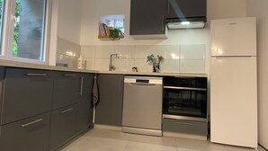 A modern kitchen with grey cabinets, a white refrigerator, a dishwasher, and an oven.