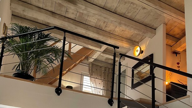 A spacious room with a high ceiling, a staircase, a dining area, and a rocking chair.