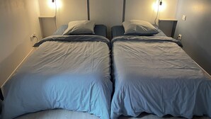A twin bed with a headboard, two bedside lamps, and a power outlet on the wall.