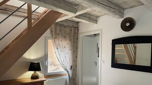 A room with a wooden staircase, a table with a lamp, a bench, a door, and a mirror on the wall.