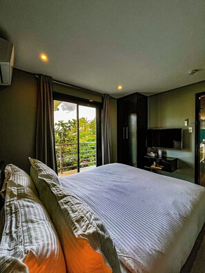 A hotel room with a large bed, a TV, and a balcony with a view of greenery. - The Pacific Coast Suites (Boracay Island)
