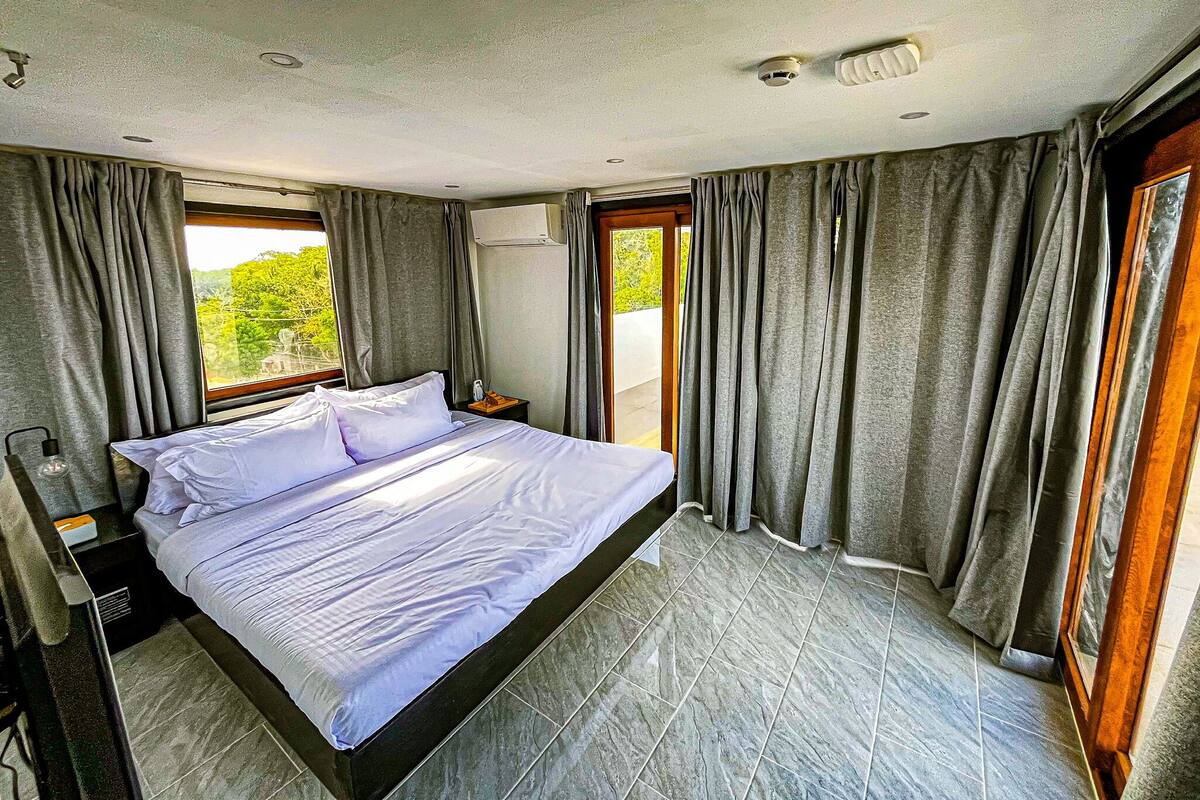 Ein Schlafzimmer mit Bett, Vorhängen, einer Klimaanlage und Blick auf Grünfläche.