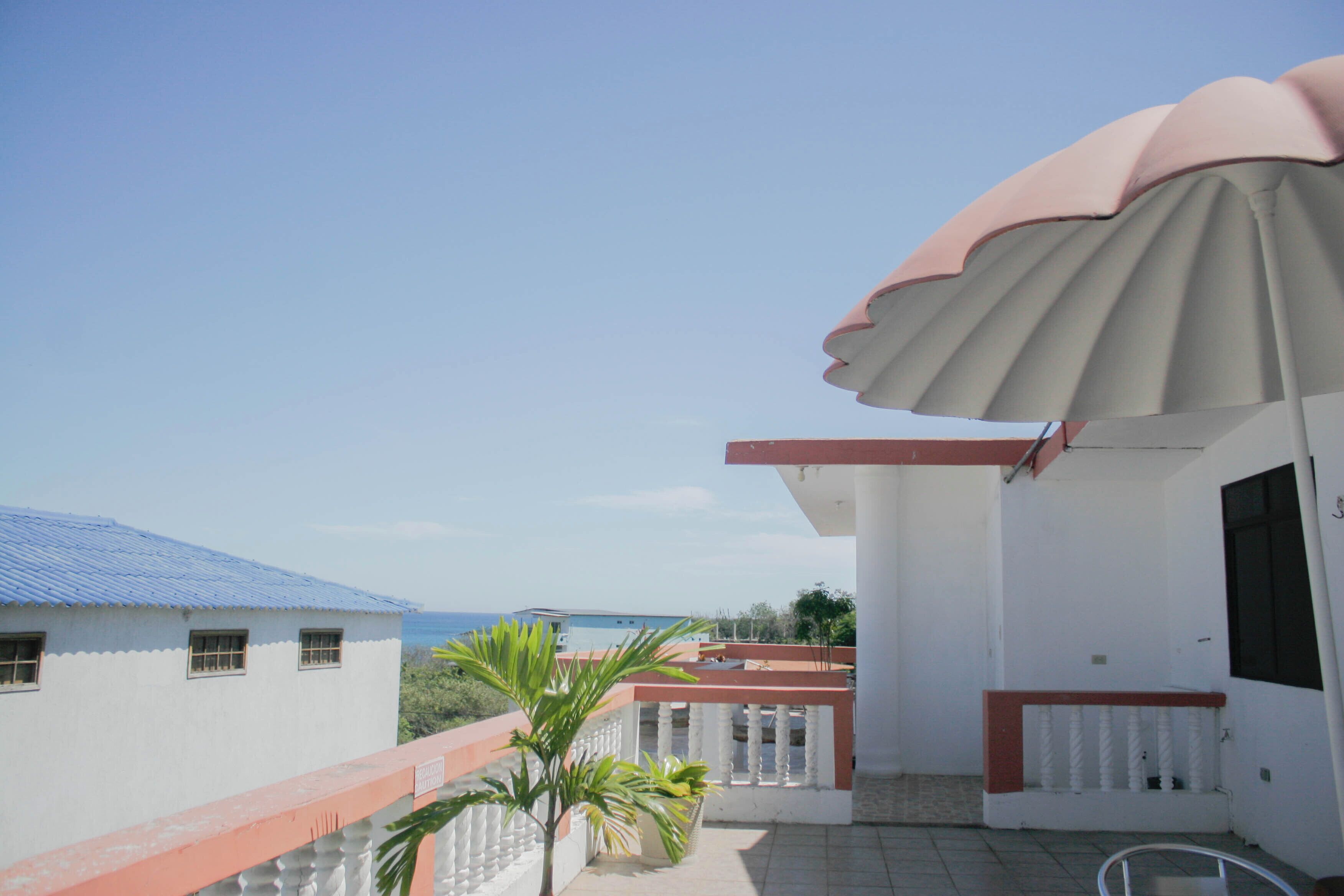 Un balcon avec une balustrade blanche, un petit palmier et une vue sur la mer.