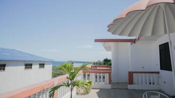 Ein Balkon mit weißer Brüstung, einer kleinen Palme und Blick auf das Meer.