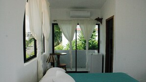 Una habitación con una cama, una mesita y un ventanal con cortinas.