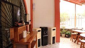 Un pequeño espacio al aire libre con mesa y sillas, un dispensador de agua y plantas en macetas.