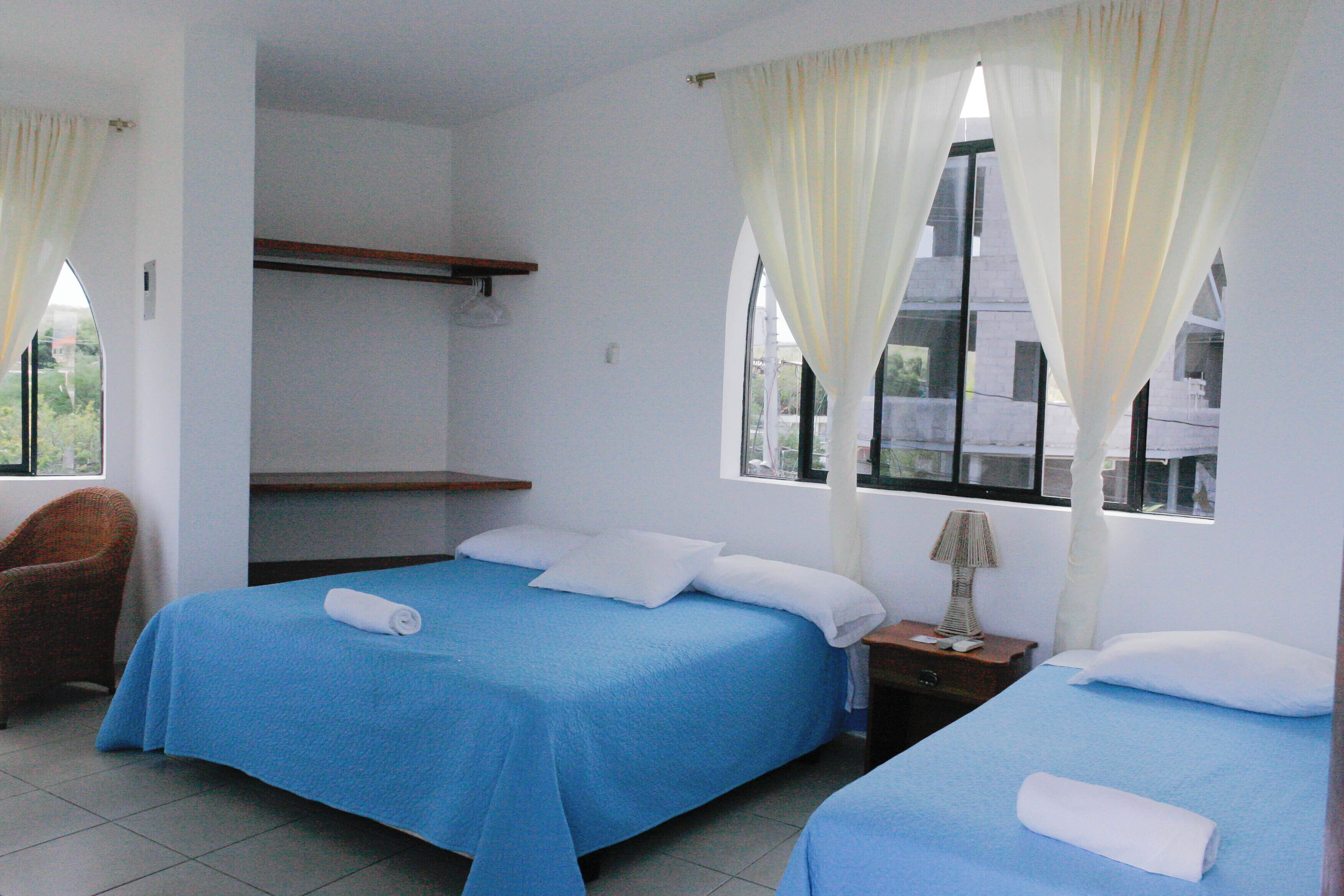 A hotel room with two beds, a chair, a nightstand, and a window with curtains.