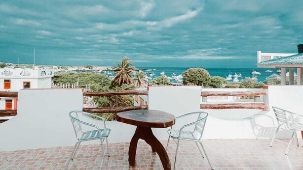 Una terraza con una mesa redonda y sillas, con vistas a un pueblo costero con barcos y vegetación.