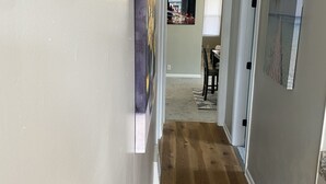 Un pasillo con suelo de madera, paredes grises y obras de arte.