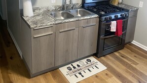 Una cocina con gabinetes grises, un lavamanos de acero inoxidable, una estufa a gas y piso de madera.
