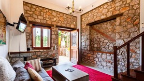 A cozy living room with a stone wall, a fireplace, a staircase, and a flat-screen TV mounted on the wall.