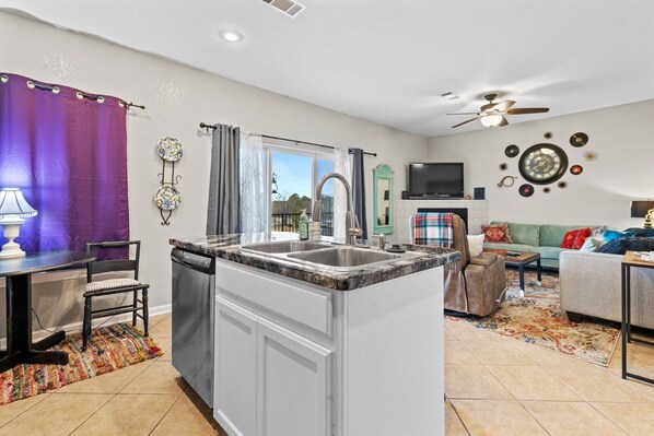 A modern kitchen with a central island, a dining area with a table and chairs, a living room with a sofa and a TV, and a ceiling fan. - 2 bed/2 bath, lake condo, ground floor, with boat slip, within 5 min. of bypass (Hot Springs)