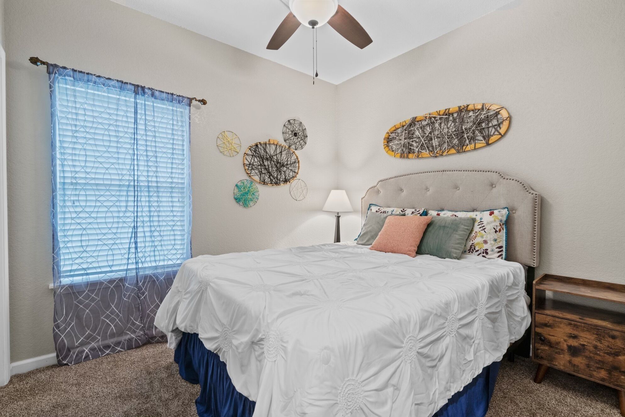 A bedroom with a bed, a ceiling fan, a window with blinds, and wall art.