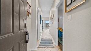 Un couloir avec une porte à gauche, un tapis sur le sol et un lit recouvert d’une couverture bleue et jaune à droite.