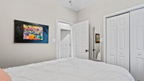 Une chambre avec un grand lit, des murs blancs et un tableau abstrait aux couleurs vives.