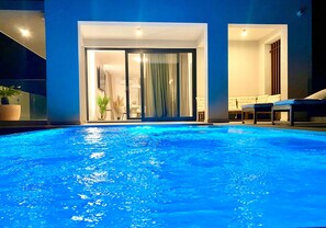 An indoor swimming pool with a glass wall leading to a room with a sofa and a lamp. - Luxurious and secluded Villa near Split- heated infinity pool with massage jets (Podstrana)