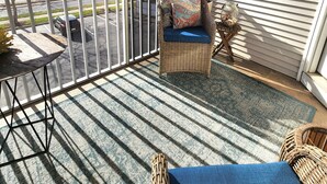 Ein sonnendurchfluteter Balkon mit Korbstuhl, kleinem Tisch und Blick auf eine Wohngegend.