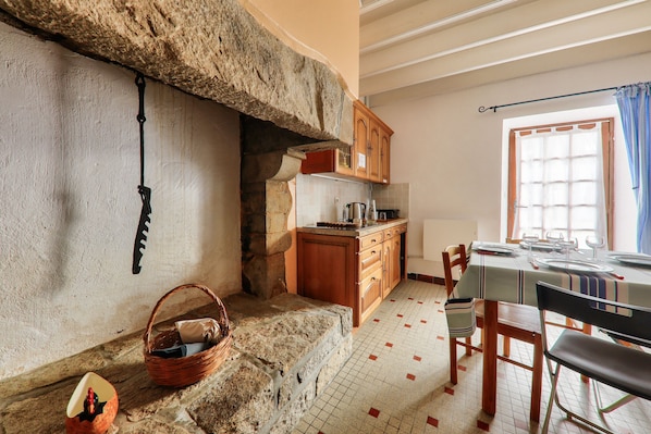 A rustic kitchen with stone walls, wooden cabinets, and a dining area with a table set for four.