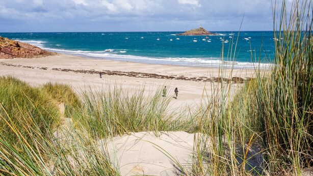 Ein Strand mit blauem Himmel, sandigem Ufer und einer fernen Felsformation.