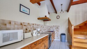 Een keuken met houten kastjes, een magnetron, een koffiezetapparaat en een prullenbak.