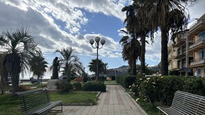 A paved walkway with benches, palm trees, a statue, and a playground.