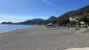 A beach with a clear sky, a few people, and buildings in the background.