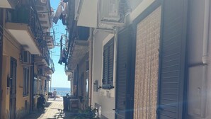 A narrow street with buildings on either side, air conditioning units, and potted plants.