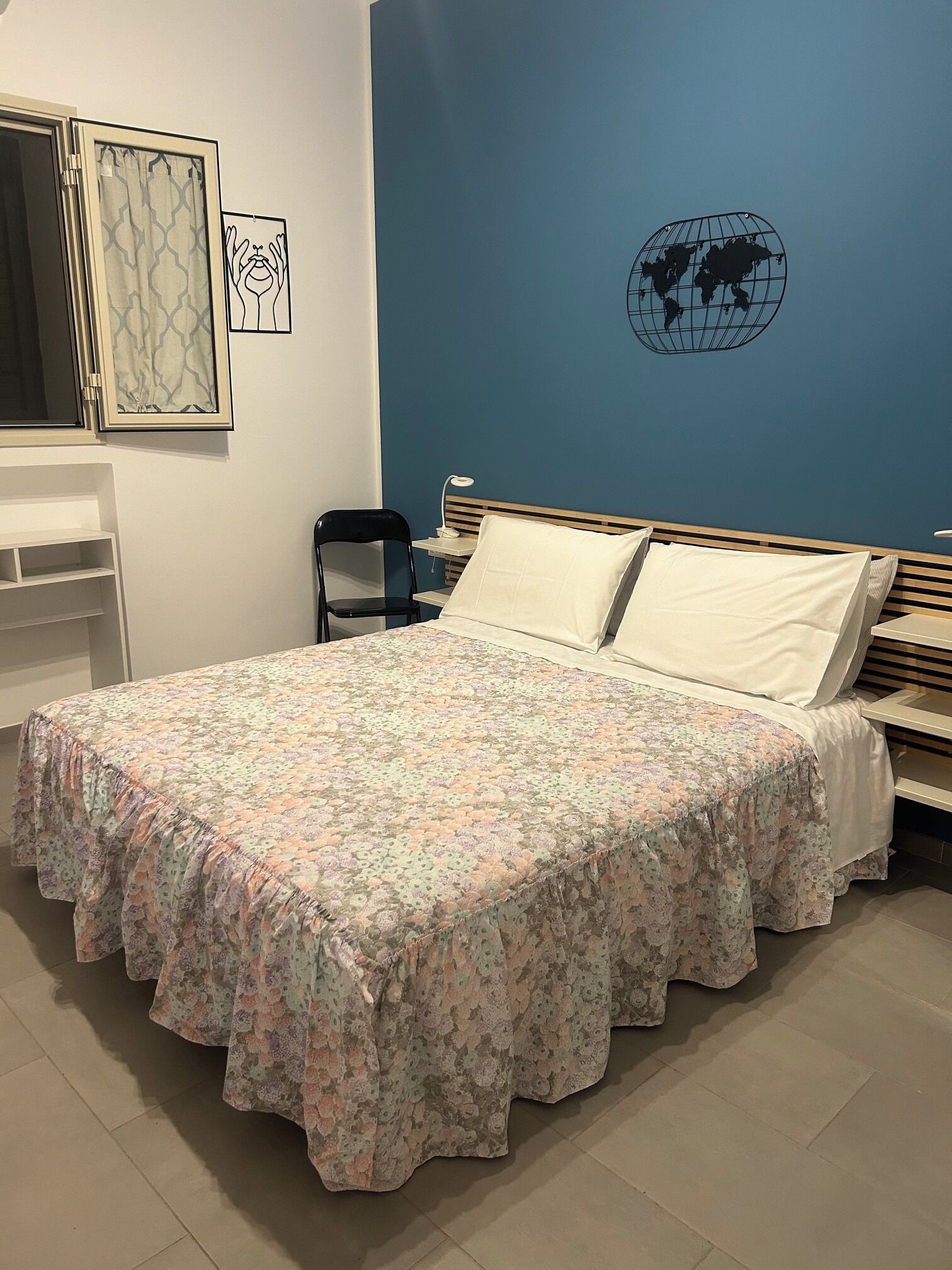 A bedroom with a bed, a desk, a chair, a world map on the wall, and a window with curtains.