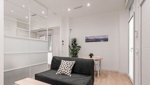 A modern, compact room with a grey sofa, a small wooden table, and a potted plant. - GuestReady - Flat near Palacio Real (Madrid)