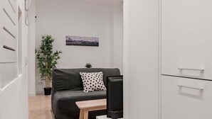 A modern, minimalist room with a grey sofa, a small wooden table, a TV, and a white wardrobe. - GuestReady - Flat near Palacio Real (Madrid)
