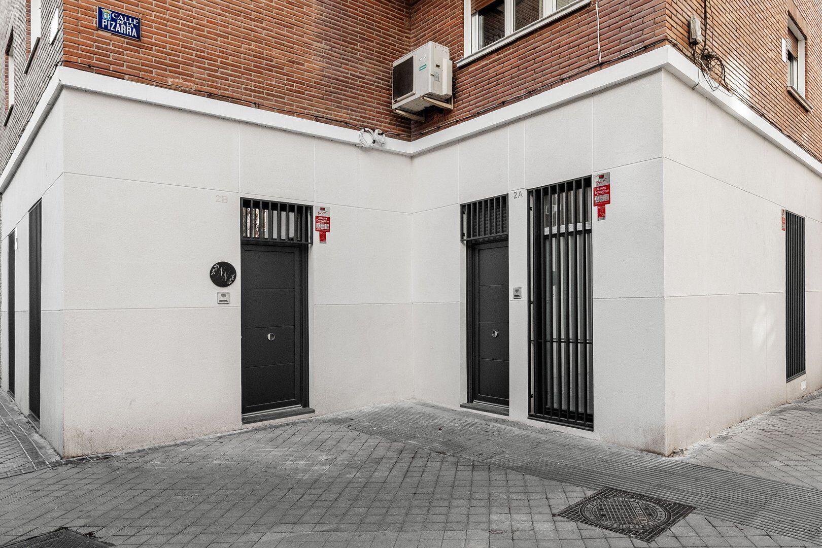 Un edificio con dos puertas negras, un detector de incendios y un cartel que dice "Calle de Pizarra".