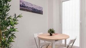A room with a round wooden table, two white chairs, a potted plant, and a cityscape painting on the wall. - GuestReady - Flat near Palacio Real (Madrid)